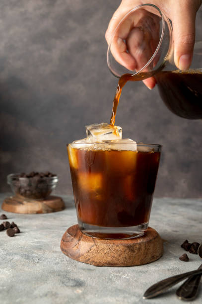 istock Pouring coffe over cup with ice cubes in glass. Preparing refreshing iced coffee 1421569704
