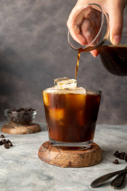 istock Pouring coffe over cup with ice cubes in glass. Preparing refreshing iced coffee 1421569706