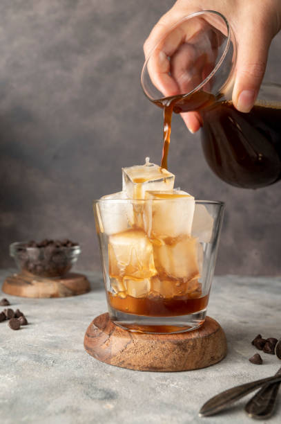 istock Pouring coffe over cup with ice cubes in glass. Preparing refreshing iced coffee 1421569707