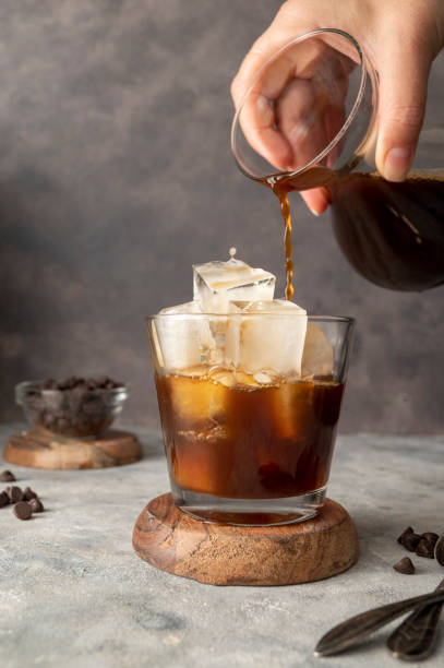 istock Pouring coffe over cup with ice cubes in glass. Preparing refreshing iced coffee 1421569740