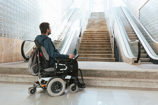 Man with disability on wheelchair stopped in front of staircase, raising awareness of architectural barriers and accessibility issues