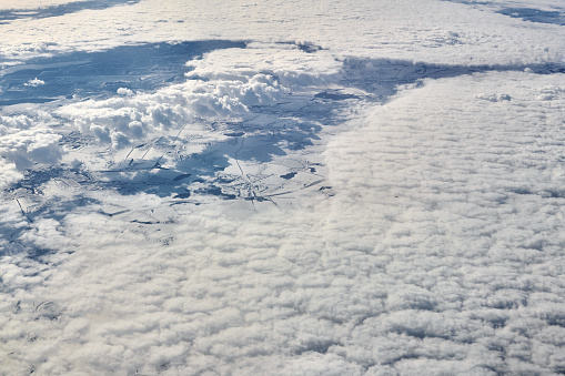 Aerial cloudscape view over top clouds to snow covered rivers, roads, cities and fields, winter fresh air. Beautiful hazed sky aerial view to Earth troposphere, snowy abstract background texture