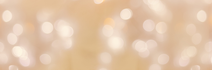 Defocused abstract bokeh background beige pastel colored, flare from lights, beige monochrome photo, blurred round bokeh as holiday fon, celebration wide banner. Glittering aesthetic textured pattern