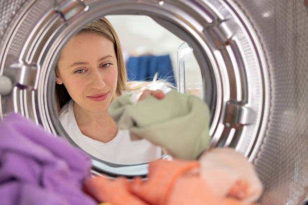 istock Woman does laundry, reaches inside washing machine, takes out colored clothes after spinning, puts dirty shirts in for washing, shot from inside drum 1421577972