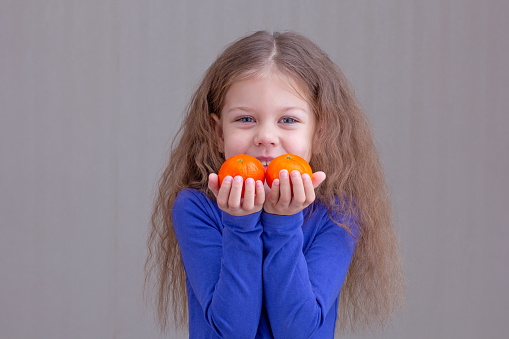 Happy and smiling child kid showing mandarins in hands on brown background looking at camera portrait of caucasian little girl of 5 years in blue