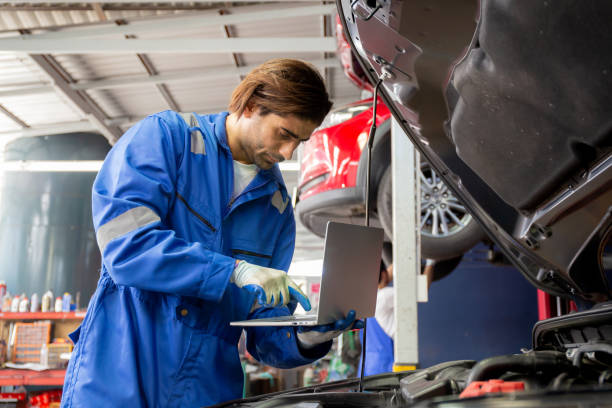 istock Young man is mechanic using laptop computer checking engine of car in the garage, worker examining and diagnostic automobile, technician and maintenance of vehicle, transport concept. 1421585250