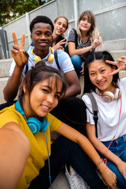 Happy smiling teen multiracial group of students looking at camera take selfie sitting on steps outside. Vertical image. Happy smiling teen multiracial group of students looking at camera take selfie sitting on steps outside. Vertical image. Education and social media concepts. teenager back to school group of people student stock pictures, royalty-free photos & images