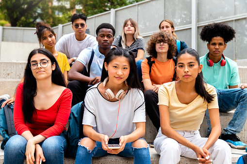 Group of multiracial teen high school students looking at camera sit on stairs outdoors. Education concept.