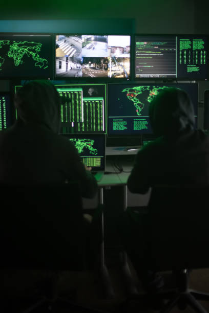 istock Two hooded hackers hacking security firewall late at night in basement hideout. Vertical image. 1421586008