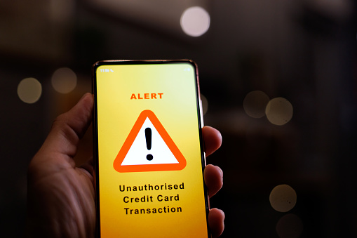 A man receiving an alert message from bank regarding unauthorised credit card transaction on his phone. Unauthorised use of is a transaction involving the charging of purchase of goods and services without the consent of the cardholder.