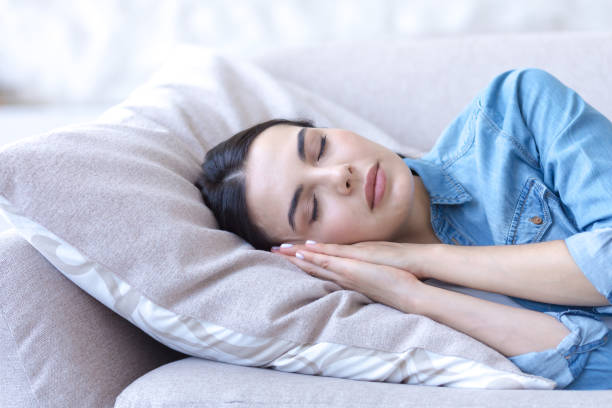istock A young woman sleeps and rests with closed eyes on a sofa on a pillow, hands folded under her head 1421588382