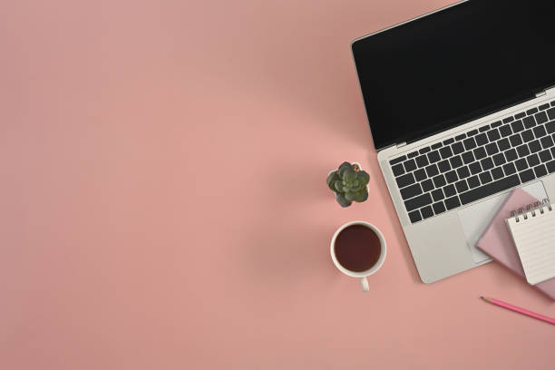 istock Modern laptop with cup of coffee and stationery on pink studio background, copy space and work place. 1421592531