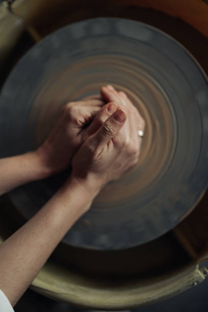 Hands of potter sculpt handmade earthenware on spinning pottery wheel in workshop closeup. Top view.