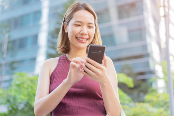 istock Close up young asian woman hand using smart phone device for social networking online or check time and date at outside city background for people with technology concept 1421596352