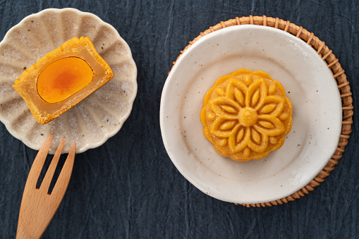 Delicious Cantonese moon cake with lotus seed pastry and salted egg yolk for Mid-Autumn Festival food mooncake on blue table background, holiday celebration serving.