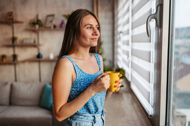 istock Young Woman Looking Out The Window And Drinking Coffee 1421598000