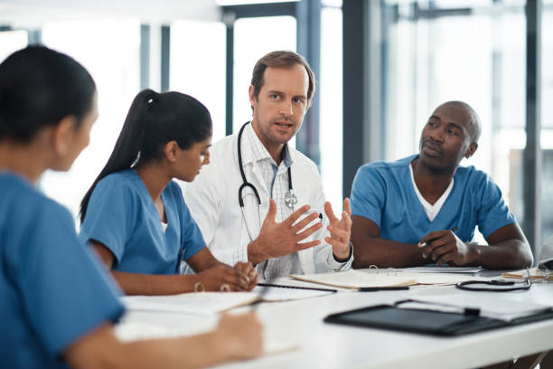 doctor conversation with nurse team, healthcare professionals meeting desk in medical boardroom office. male registrar talking hospital job, world health day communication and people working together - board room discussion contract agreement imagens e fotografias de stock