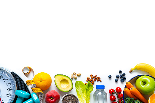 Overhead view of a composition of healthy food, weight scale, tape measure and dumbbells shot on white background. The composition is at the bottom of an horizontal frame making a border and leaving copy space.  High resolution 42Mp studio digital capture taken with SONY A7rII and Zeiss Batis 40mm F2.0 CF lens