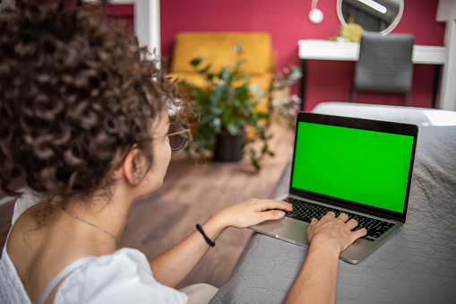 A young teenage girl works on a green screen device, Key Screen Stand, an ideal background for adding various messages to the screen.