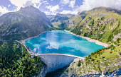 Water dam and reservoir lake in Swiss Alps mountains producing sustainable hydropower, hydroelectricity generation, renewable energy to limit global warming, aerial view, decarbonize, summer