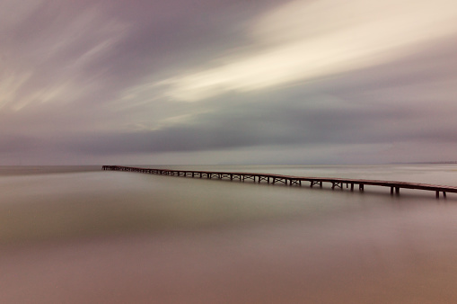 Long exposure landscape on the beach with wooden bridge. Side view of a wooden pier on a calm beach at sunset