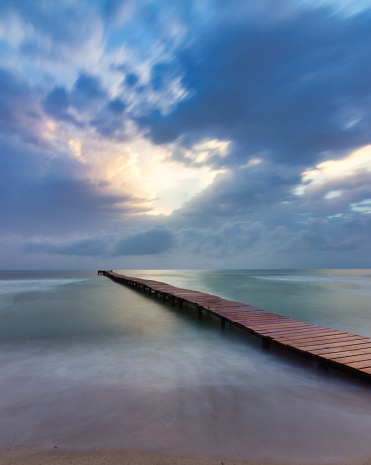 Long exposure of a wooden bridge in the ocean at blue hour. A wooden bridge leading to the ocean at sunset