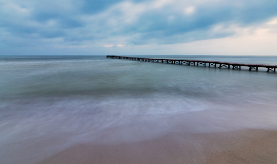 Side view of a wooden pier on a calm beach at sunset. Long exposure landscape on the beach with wooden bridge