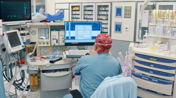 Anesthesiologist looking at a patient's vital signs monitor during surgery stock photo