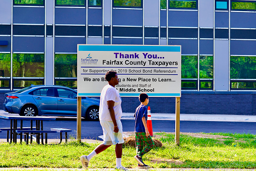 Fairfax, Virginia, USA - August 31, 2022: Two students walk past a sign outside Robert Frost Middle School thanking citizens for their taxes being used to renovate the school.