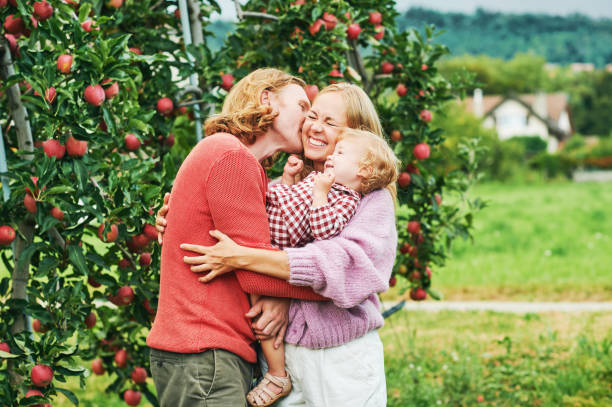 Outdoor portrait of happy young family with toddler kid girl, enjoying nice day in apple orchard stock photo