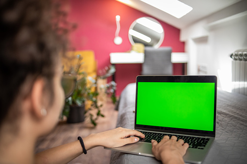 A young teenage girl works on a green screen device, Key Screen Stand, an ideal background for adding various messages to the screen.