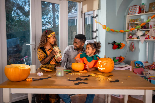 Look What I Made! A man and his daughters sitting at their kitchen table at home in North East England during halloween, designing and carving pumpkins. One girl is showing her father and sister a butternut squash that she has designed for the halloween season. pumpkin decorating stock pictures, royalty-free photos & images