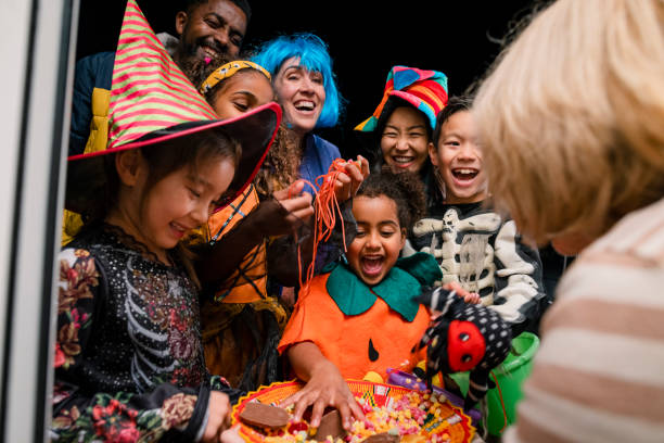 Candy for the Kids Taken from inside a residential house, two families wearing fancy dress, out trick or treating in North East England during halloween. The children are taking sweets off a plate that an unrecognisable woman is holding. trick or treat stock pictures, royalty-free photos & images