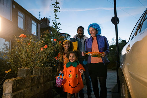 A family wearing fancy dress, out trick or treating in North East England during halloween. They are walking on a footpath together while carrying buckets and trays, ready to collect sweets from neighbours houses.