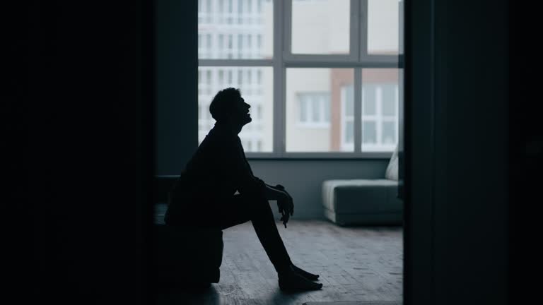 Stressed caucasian middle-aged man sitting on the sofa in bedroom while get bad news from mobile phone. Depressed and hopeless male being alone with negative emotion.