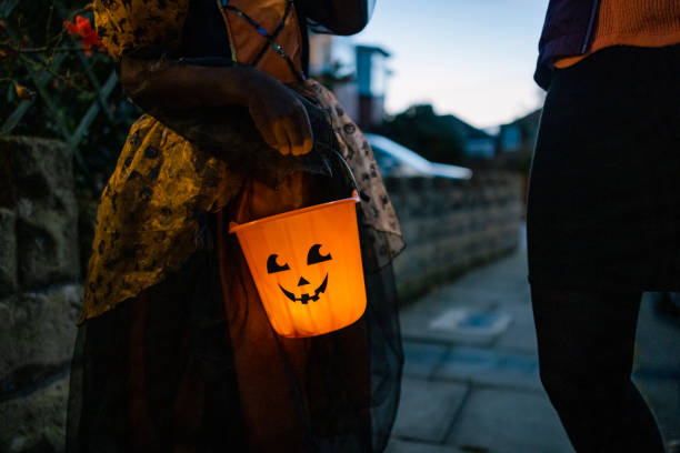 All of a Glow An unrecognisable girl holding a glowing orange bucket with a spooky face on it while standing on a residential street in North East England. She is ready to go trick or treating and collect sweets. trick or treat stock pictures, royalty-free photos & images