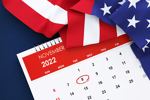 US Midterm Elections Concept - 2022 November Calendar Sitting Behind Rippled American Flag On Blue Background