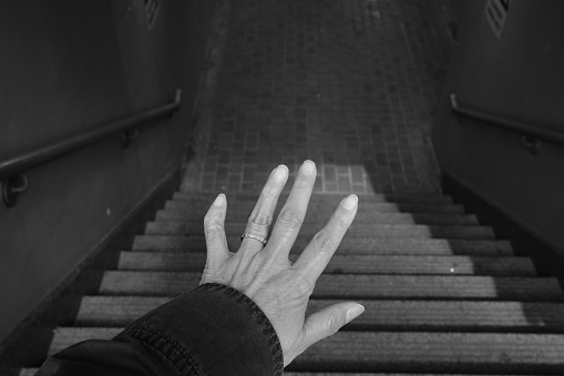 A hand reaching out over a dark staircase.