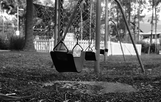 Children's swing sets at a park after rain with a puddle underneath.