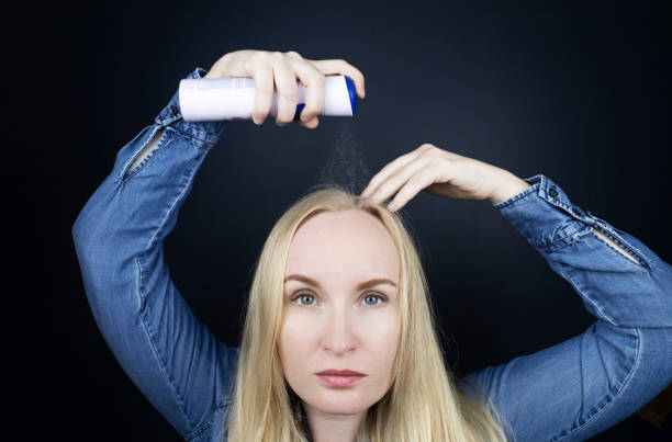 Dry shampoo. Blonde girl sprays shampoo on her hair. The problem of oily hair while traveling. An emergency remedy for excessive sebum production. Make your head clean without water stock photo