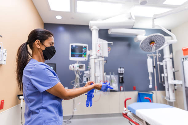 Mature female nurse dons protective gloves for shift in ER A profile view of a mature adult nurse as she puts on protective gloves before attending to patients in the emergency room. surgical light stock pictures, royalty-free photos & images