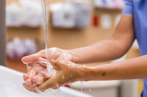 A close up photo of water pouring over a healthcare worker's hands as she cleans and sanitizes them before examining a patient.