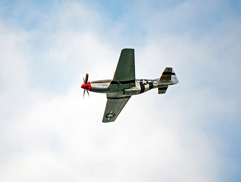 American P-51 Mustang fighter, Bournemouth, England. The North American Aviation P-51 Mustang was an American single seat, long-range, fighter and fighter-bomber used during conflicts such as World War II and the Korean War, seen here in flight over open sea with cumulus cloud formation in blue sky