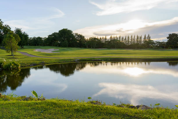 blick auf den golfplatz mit fairway und teich bei sonnenuntergang, golfplatz mit einem reichen grünen rasen schöne landschaft, grünes gras und wälder auf einem golfplatz - golf putting golf course golf club stock-fotos und bilder