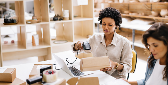 Online store owner scanning the barcode of a package box in a warehouse. Creative young businesswoman preparing an order for shipping. Female entrepreneurs running an e-commerce small business.