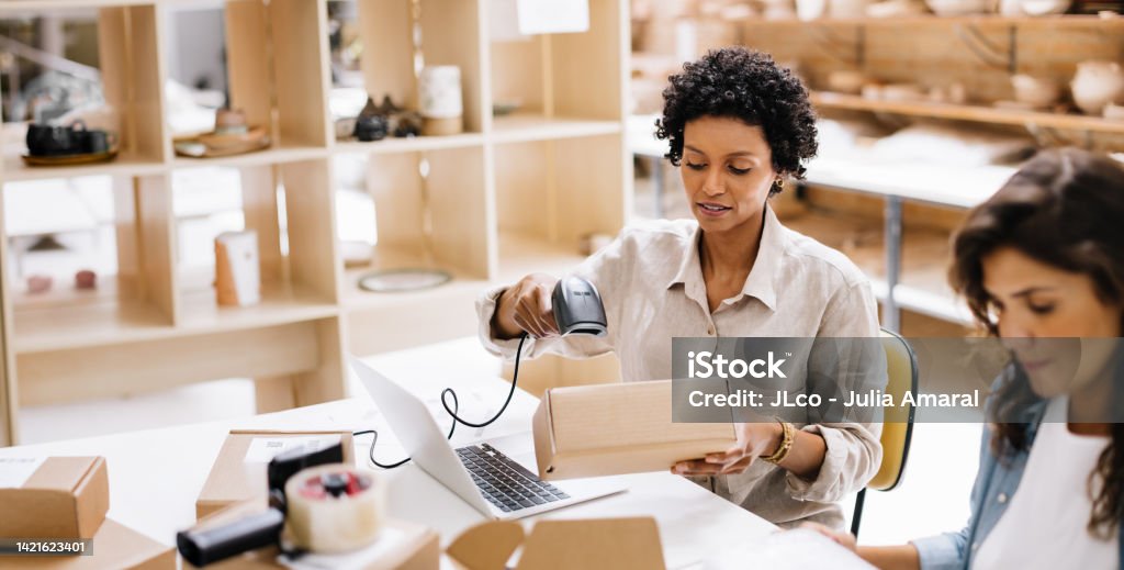 Online store owner scanning the barcode of a package box in a warehouse Online store owner scanning the barcode of a package box in a warehouse. Creative young businesswoman preparing an order for shipping. Female entrepreneurs running an e-commerce small business. E-commerce Stock Photo