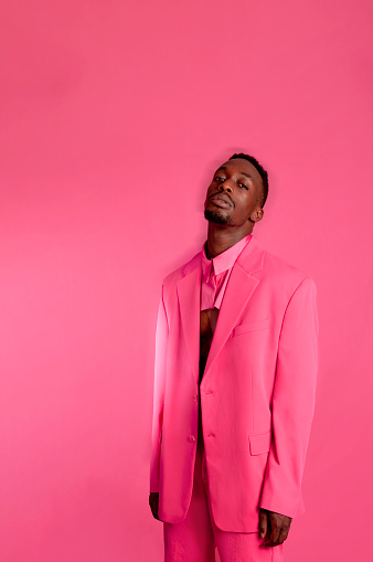 A fashionable black man model wears pink suit on fuchsia background Motion effect. Vertical photo