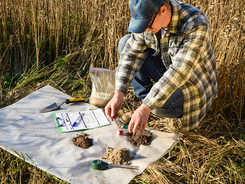 Closeup of agronomy specialist preparing soil samples for laboratory analysis outdoors. Professional farmer filling sample bag with material sampling at field. Environment research, soil certification
