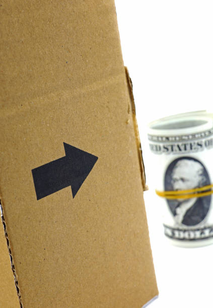 istock cardboard box with arrow sign and rolled dollars 1421628114