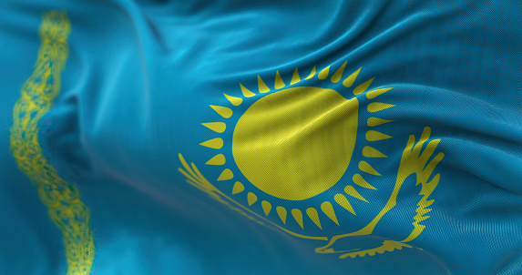 Close-up view of the Kazakhstan national flag waving in the wind. Kazakhstan is a transcontinental country located mainly in Asia and partly in Europe. Fabric textured background. Selective focus